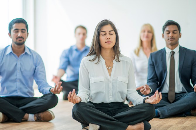 group-of-coworkers-sitting-cross-legged-with-eyes-closed-while-meditating-on-floor
