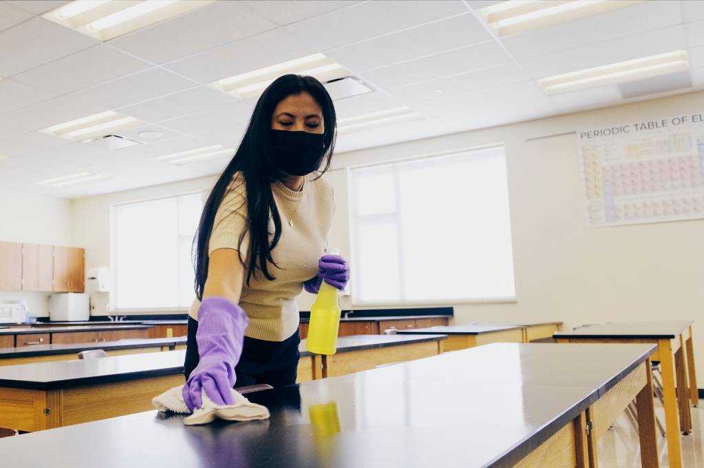 teacher-wearing-purple-rubber-gloves-cleaning-her-science-classroom-tables-with-cleaning-solution-and-cloth
