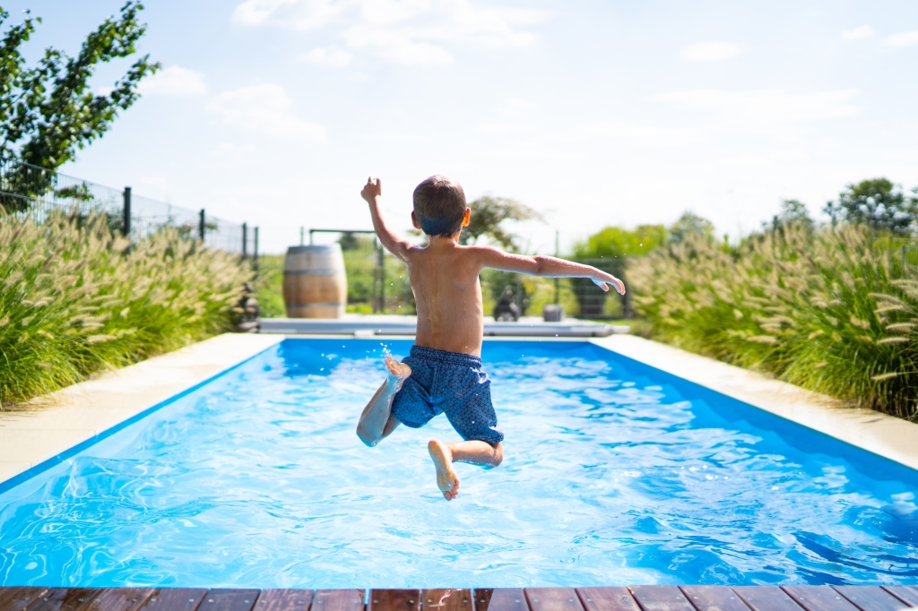snapshot-of-young-boy-wearing-blue-swim-trunks-jumping-into-pool-on-hot-summer-day