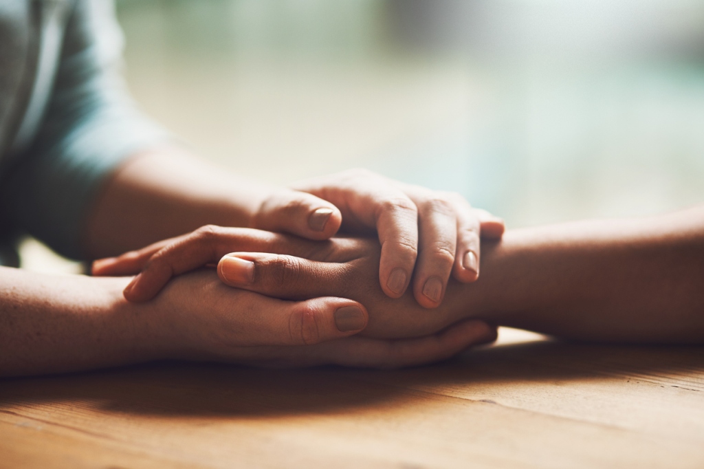 Shot of two people holding hands in comfort - concept of suicide risk screening.