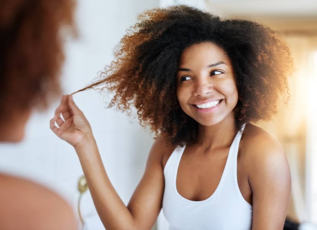 Smiling woman looking at her reflection in the mirror while touching her healthy hair - solving common hair problems.