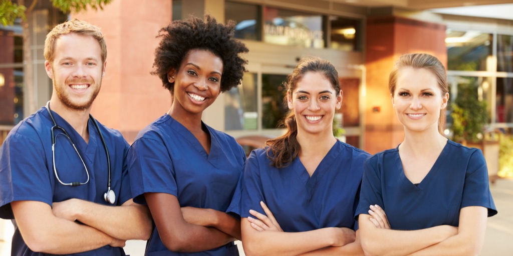 one man and three women wearing blue scrubs standing in a line with arms crossed and smiling