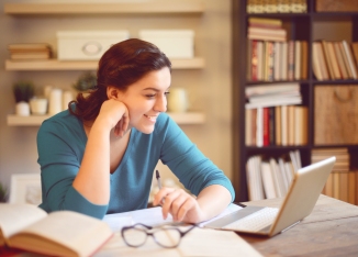 woman smiling while sitting at table and working on online medical course at home