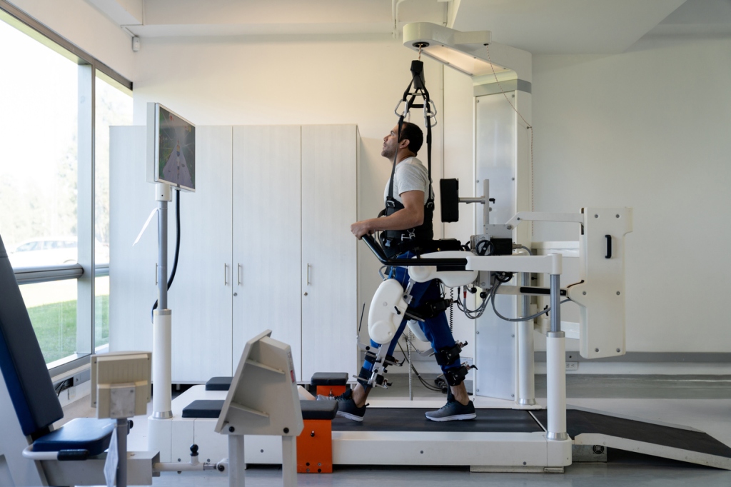 A man doing physical therapy by using an exoskeleton to walk on a treadmill